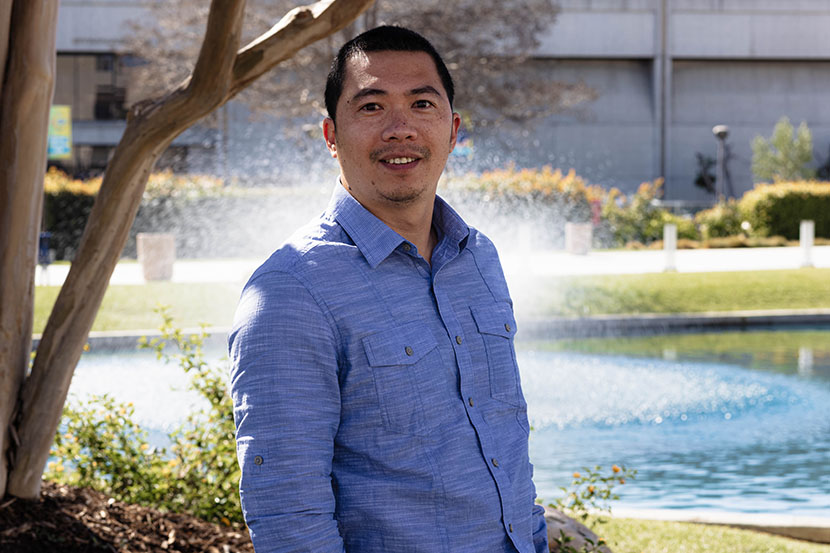 Dual Enrollment Khanh Cao wearing blue button down shirt standing with pond behind him