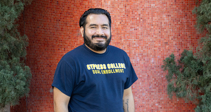 Dual Enrollment staff Pablo Aguilar smiling with red tile wall behind him