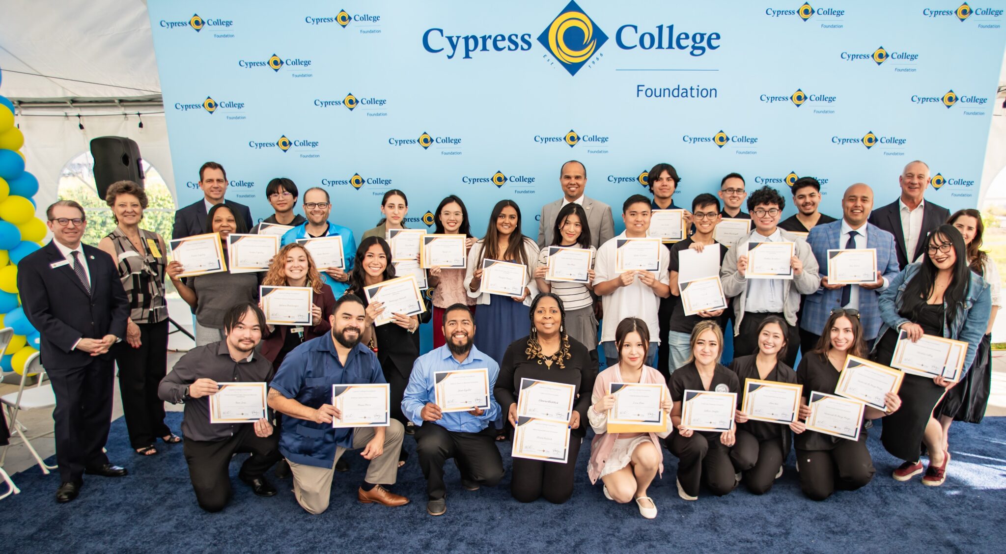 About 20 students smile and hold certificates