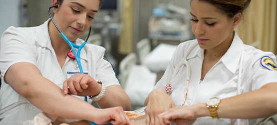 Students dressed in nursing attire attending to a patient