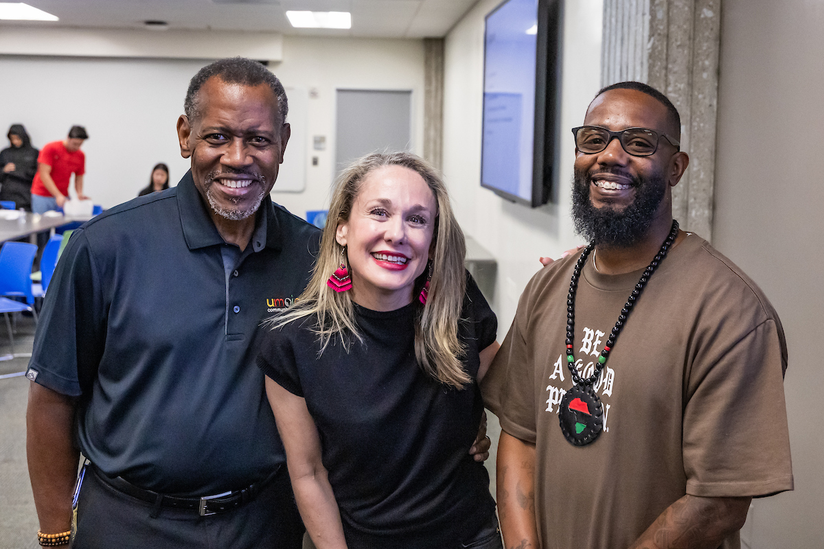 Two Black men and one light-skinned woman face the camera and smile .