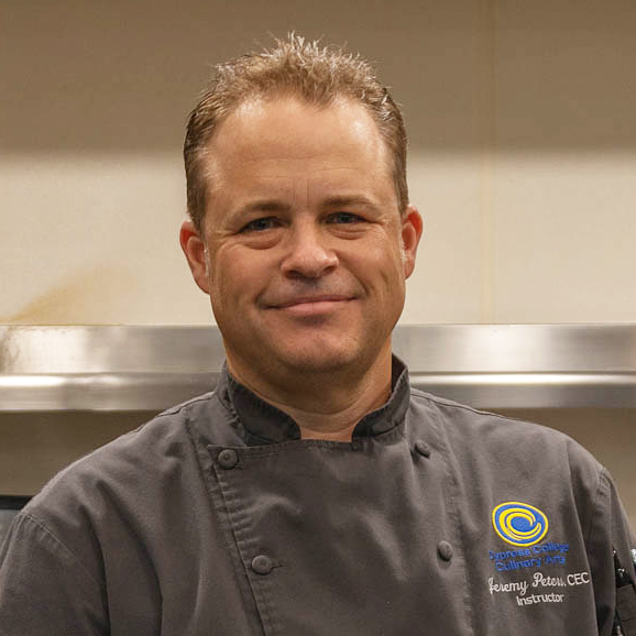 A man with a tight smile wears a chef's jacket.