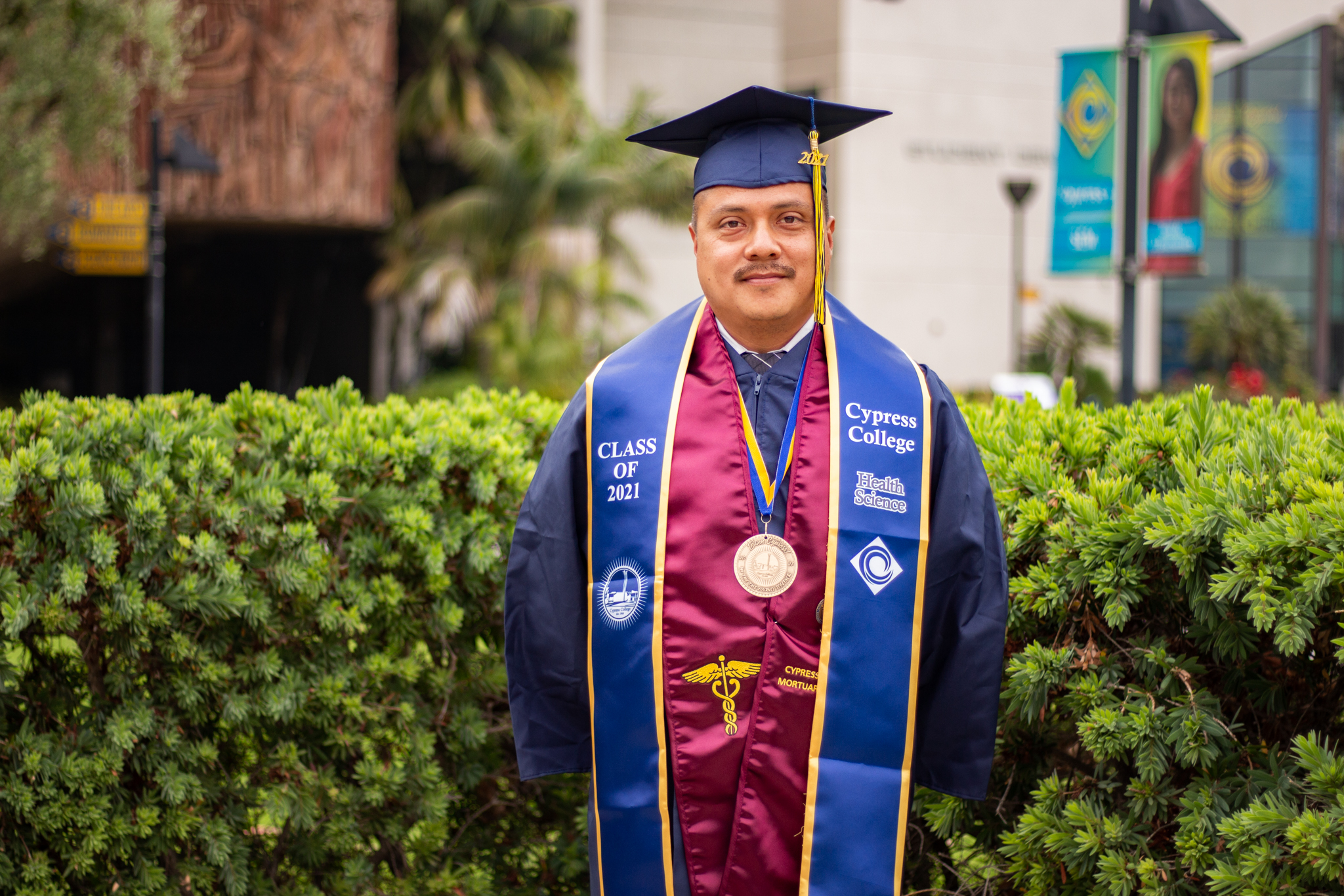 David Garcia wears graduation regalia in front of greenery on the Cypress College campus.