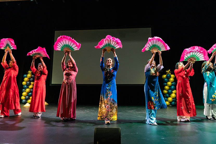 Dancers in colorful Lunar New Year costumes holding fans on stage