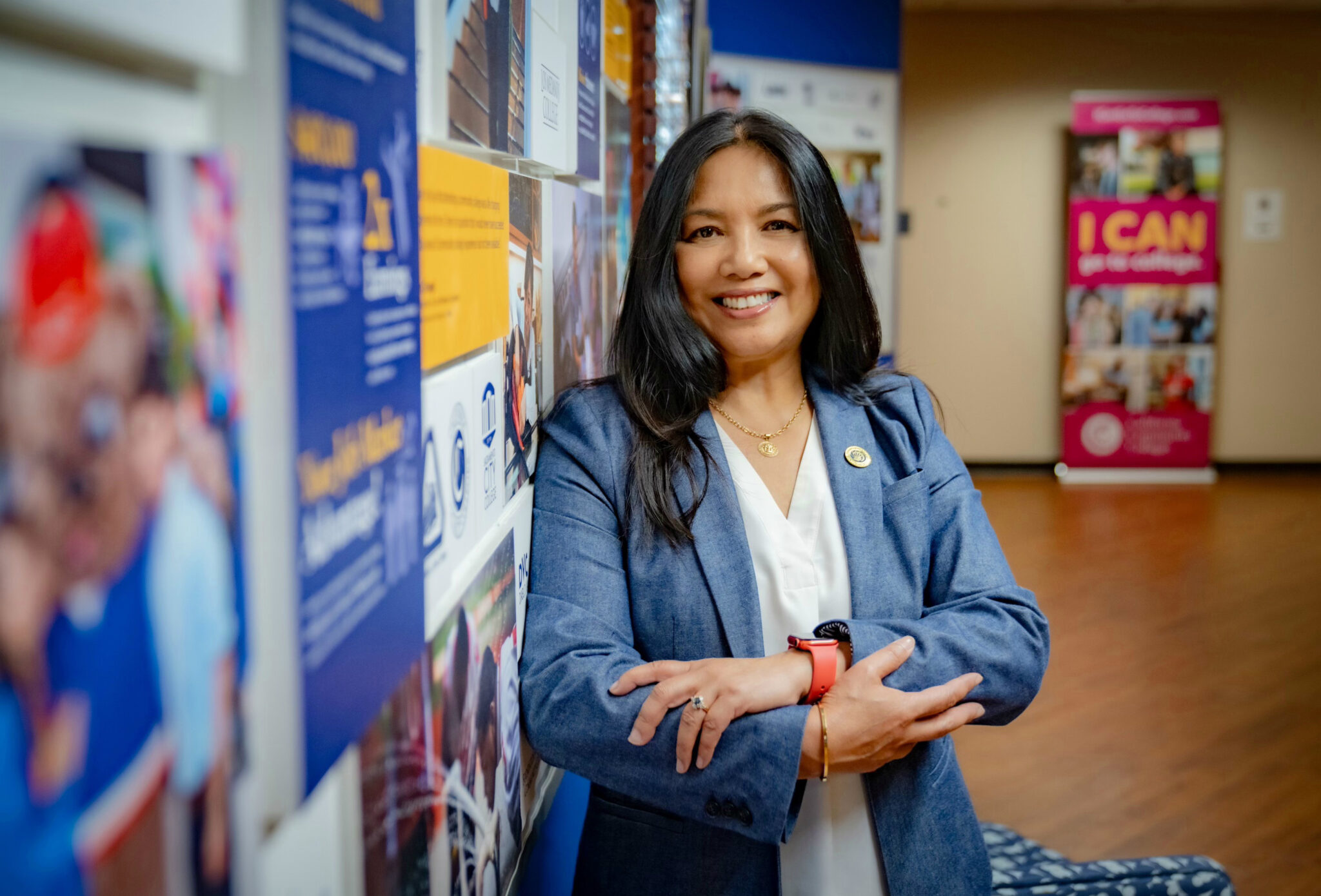 Woman with long dark straight hair stands with arms folded in front of posters