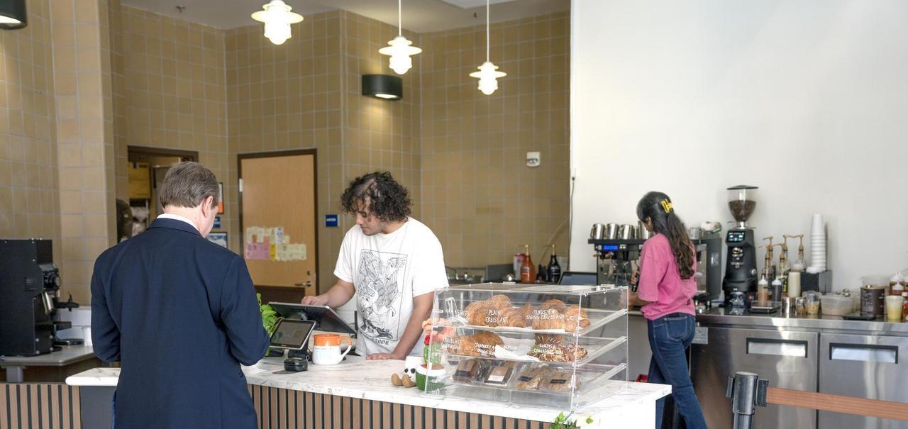 Customer interacts with barista at the counter in the Cypress College coffee shop, while another person selects items from a pastry display.