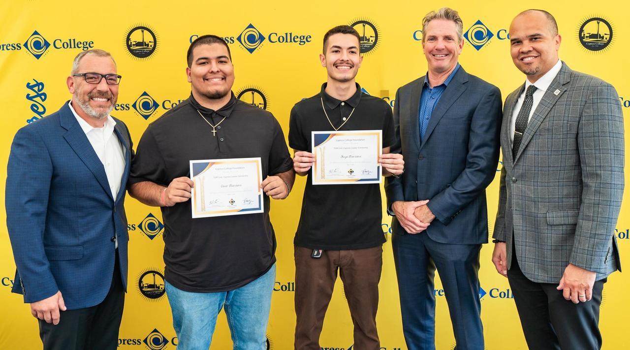 Students holding up scholarship awards in front of a yellow background with the Cypress College logo