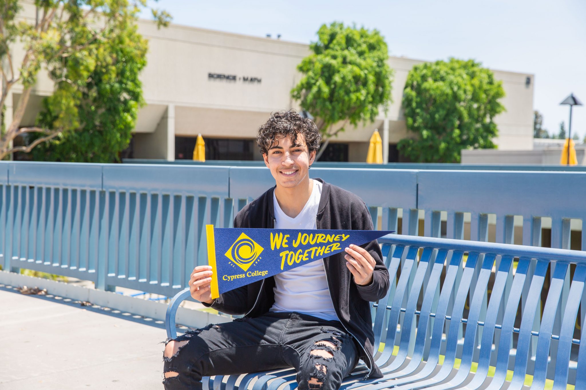 Student Nader Barsoum holding a pennant and sitting on a bench on campus