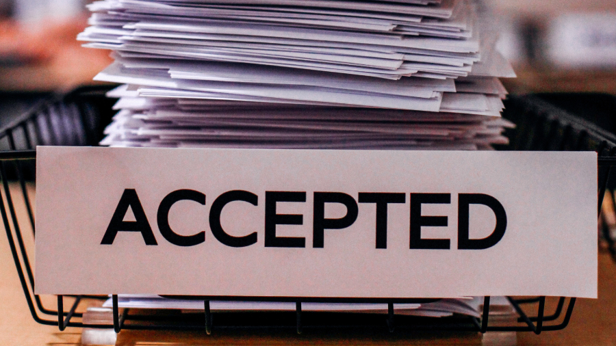 Stack of papers in bin labeled "Accepted"