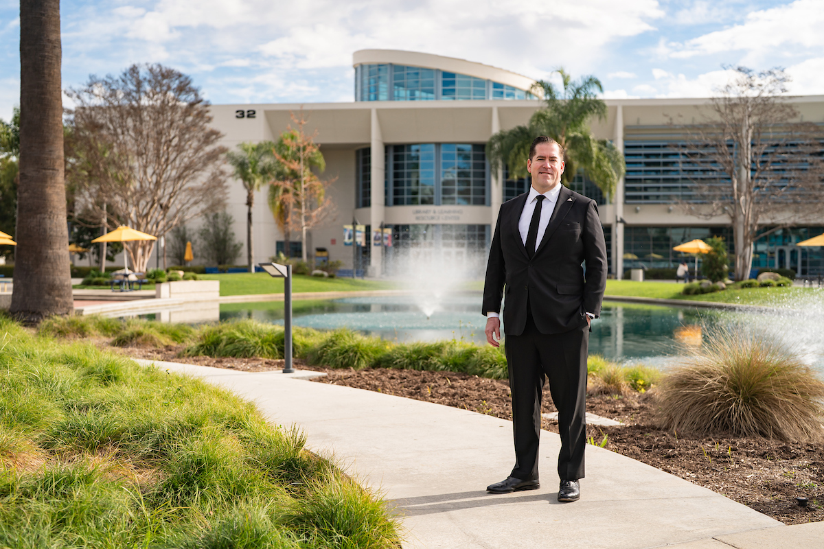 A man in a dark suit stands in front of campus pond