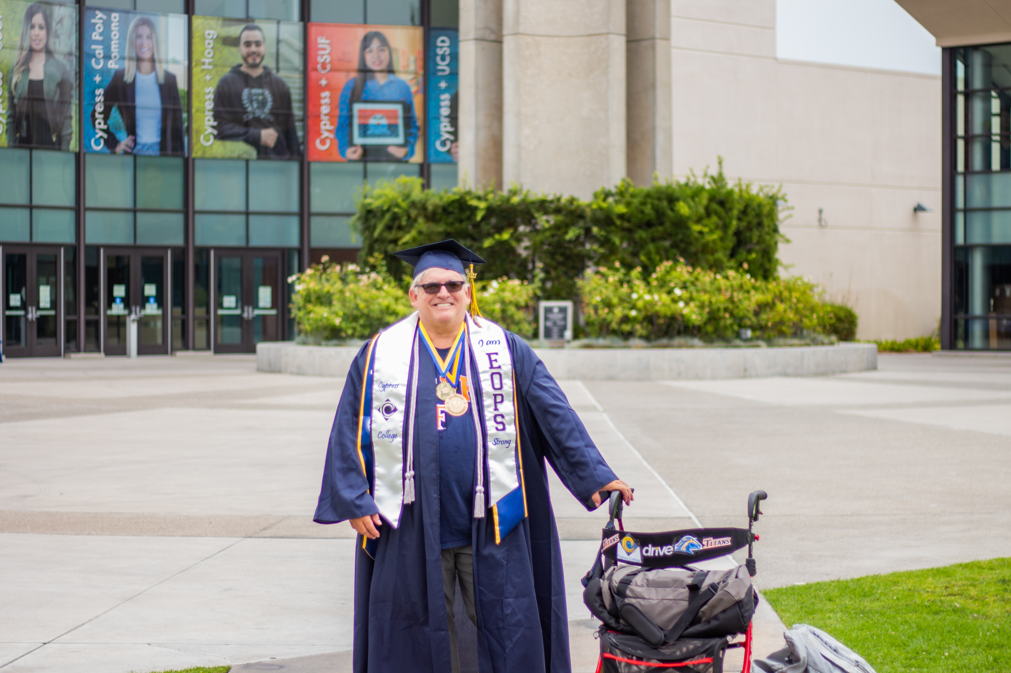 Patrick Hale poses in front of Cypress College Student Life and Leadership building with his graduation regalia and walker.