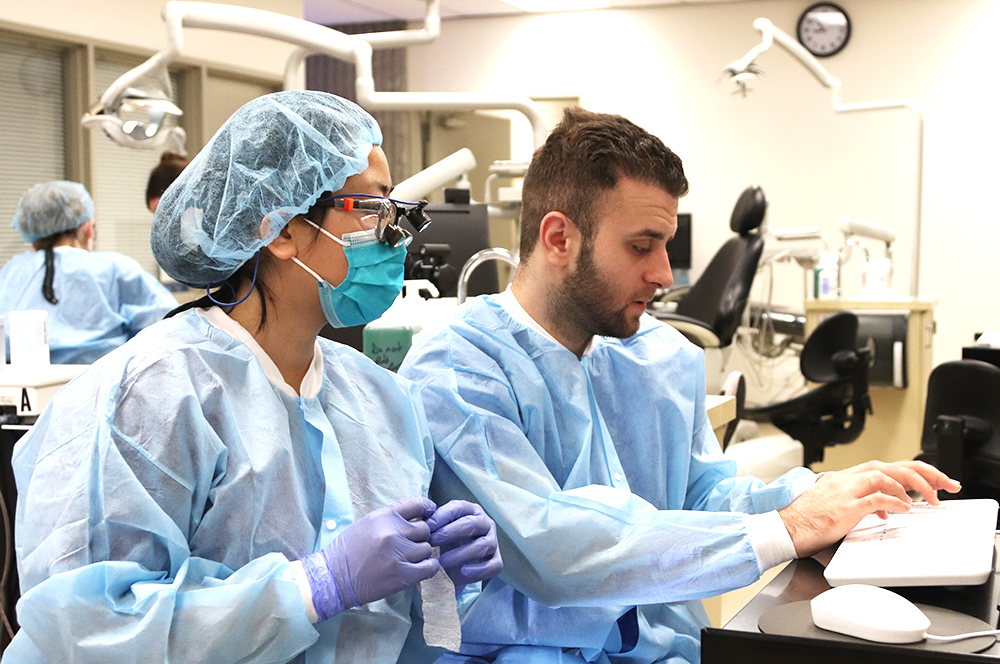 Two Dental Hygiene program students wear scrubs and enter data in the Dental Hygiene clinic.