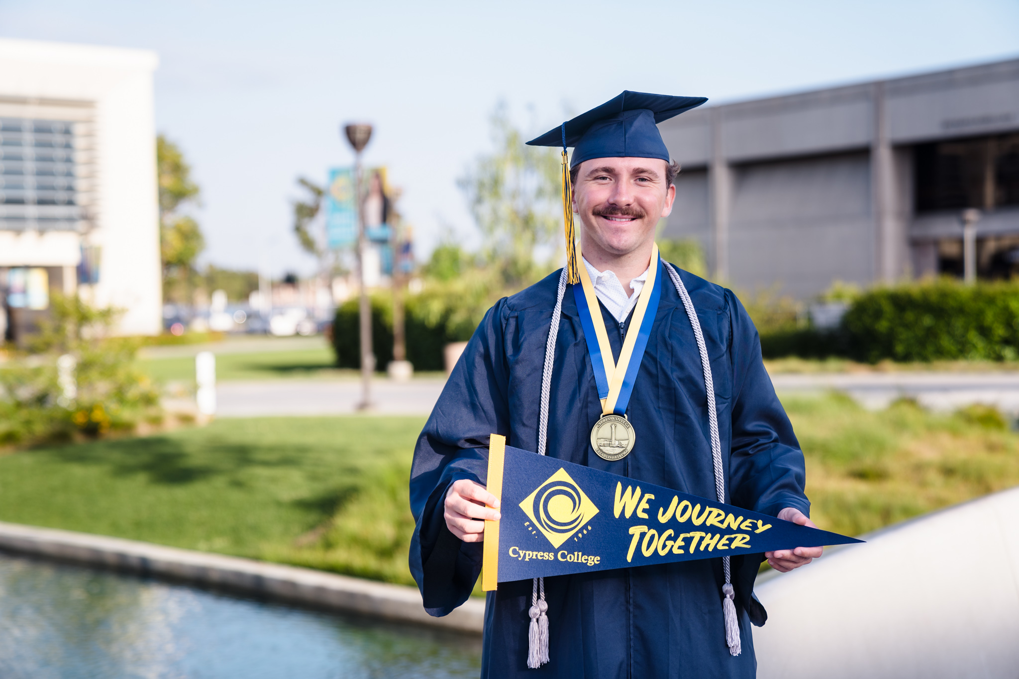Student Garrett Deiro stands in front of a Cypress College building while wearing graduation regalia.