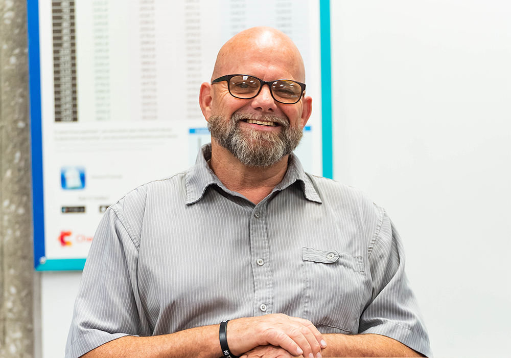 A bearded man with a shaved head smiles at the camera.