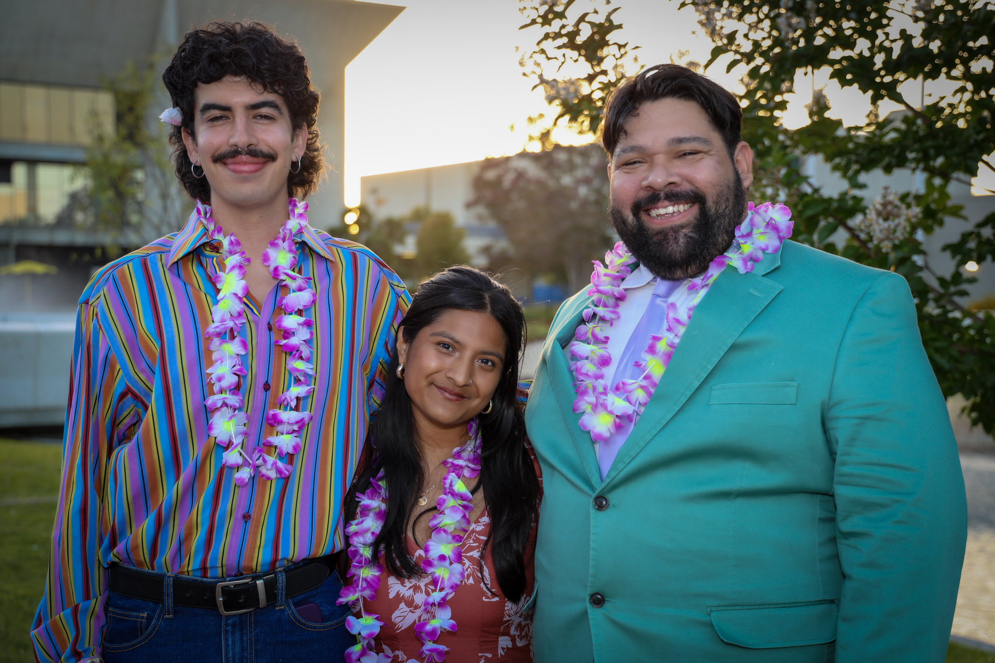 Three people wear leis and pose for the camera