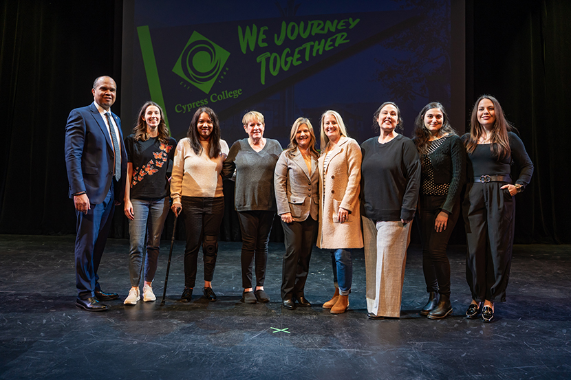 Group of individuals posed on a stage, showcasing a banner that reads "We Journey Together," representing Cypress College.