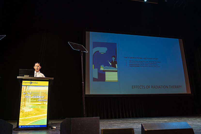 A speaker presents on radiation therapy effects at a podium, with a slide depicting a treatment process. Stage setup includes microphones and screens.