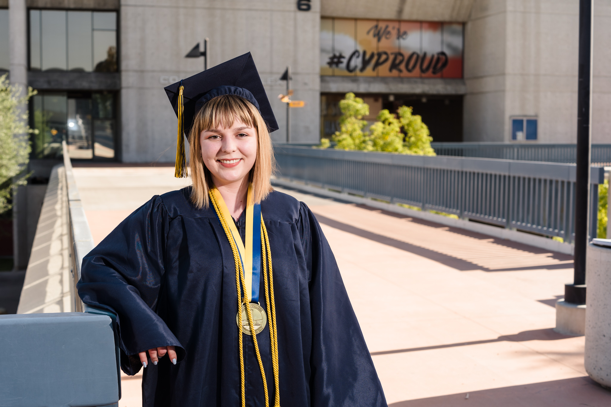 Student Bradi Palomarez stands in front of the Science and Math building on campus, wearing graduation regalia.