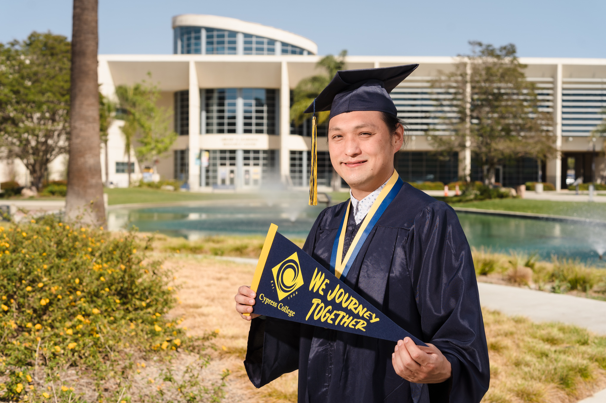 Culinary Arts student Dan Kim poses in graduation regalia in front of gonfalons for Cypress College and Career Technical Education