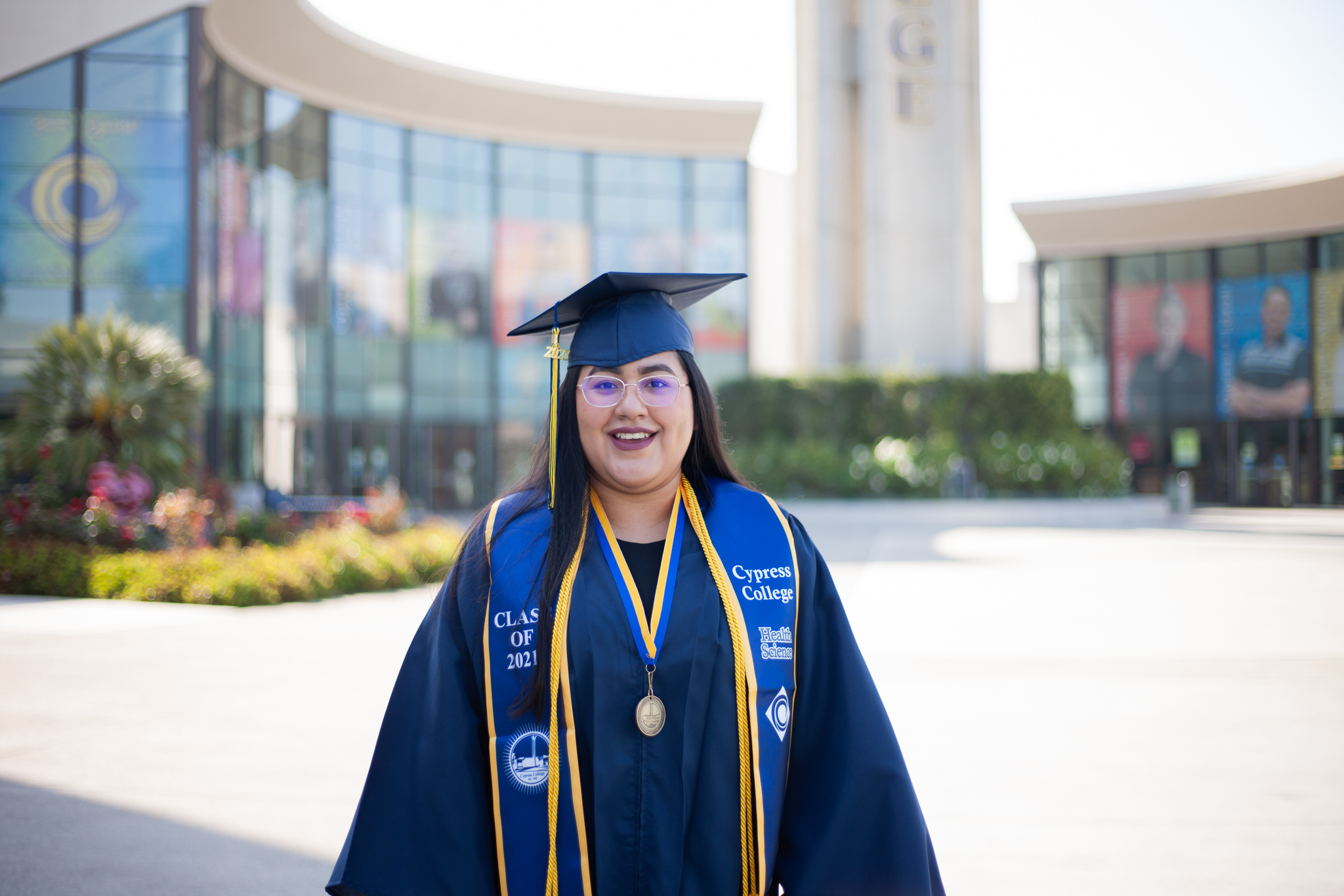 Abigail Villegas stands in front of the campanile wearing graduation regalia. 