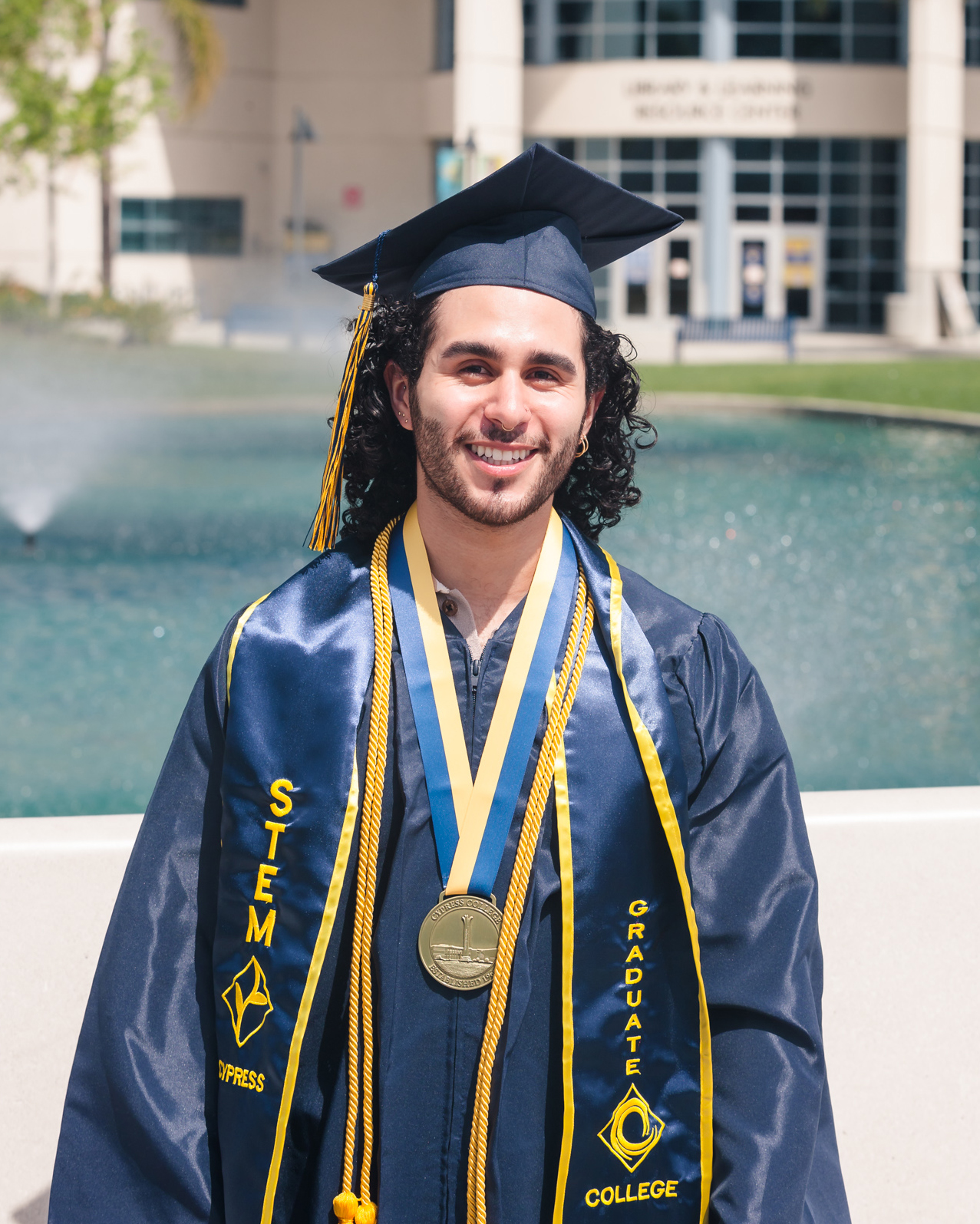 Student Justin Urquilla poses in front of library wearing Cypress College graduation regalia.
