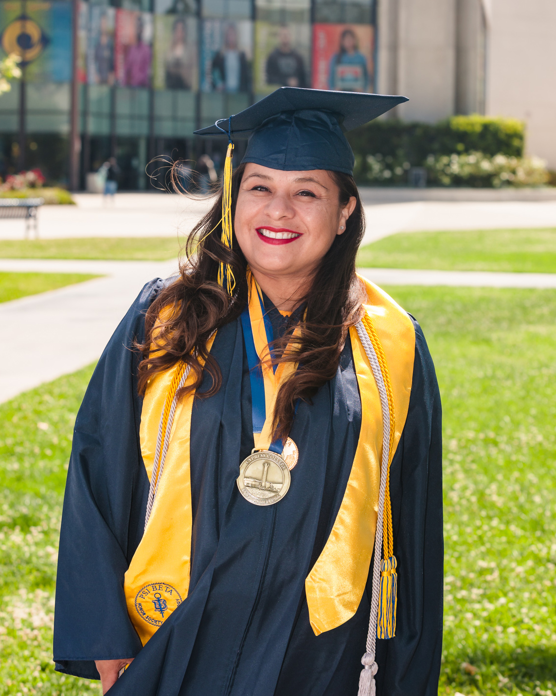 Student Mireya Alt poses in front of Cypress College Student Center while wearing graduation regalia.