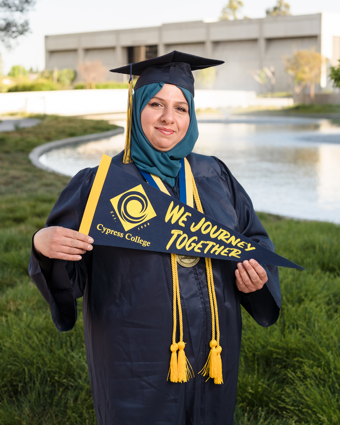 Student Rasha Jasim poses in front of the Cypress College pond wearing graduation regalia.