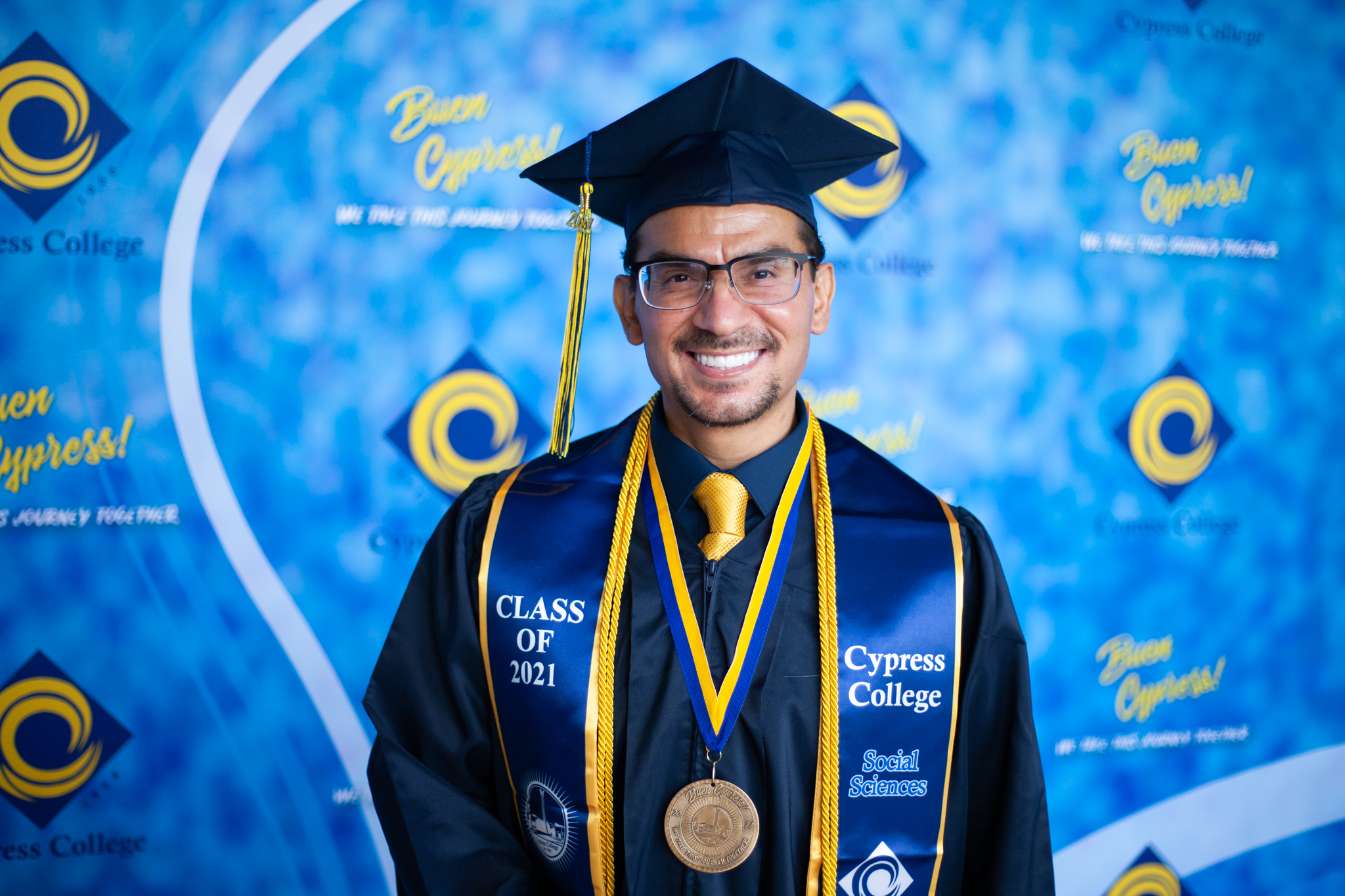 Social Sciences student Wilfredo Carrasco poses in front of blue background.