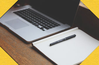 Laptop computer on a desk, along with a notepad and pen