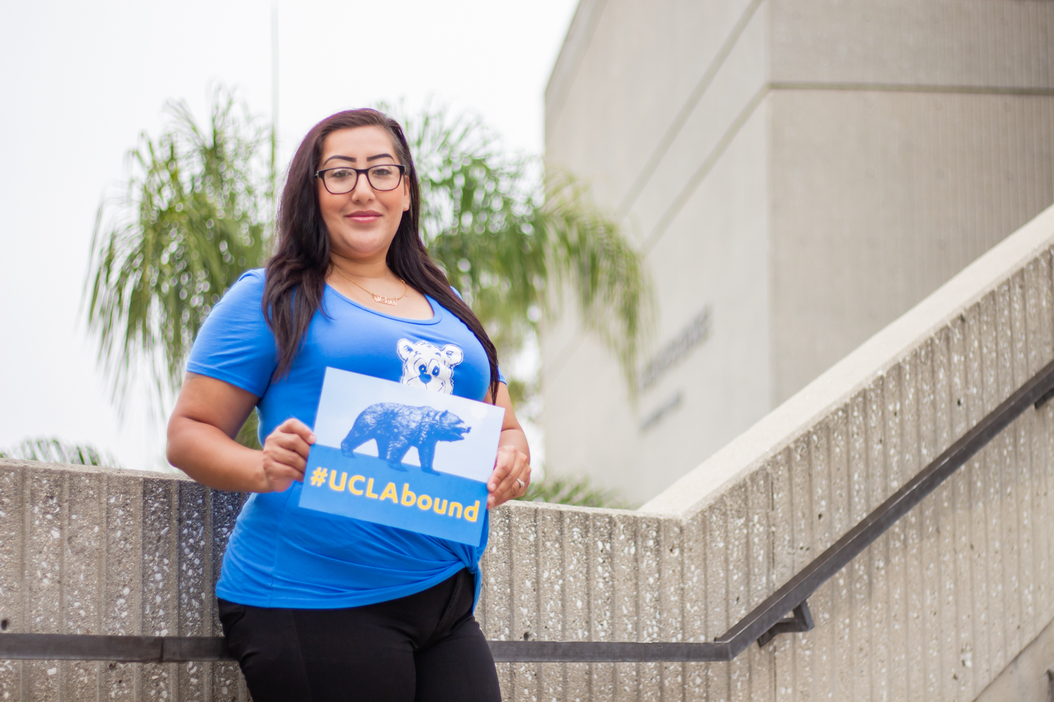 Cypress College student Melissa Whitewwater poses on the steps leading to a campus building and holds a UCLA bound sign.