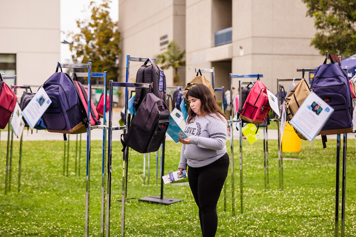 A student reads a story clipped to a backpack in Gateway Plaza.