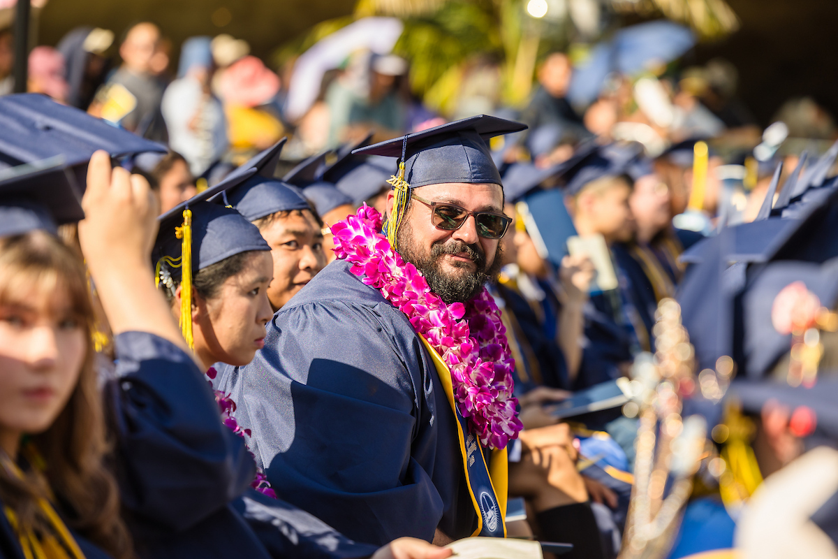 A man in sunglasses and a flower lei smiles from the audience of the 58th Cypress College commencement ceremony