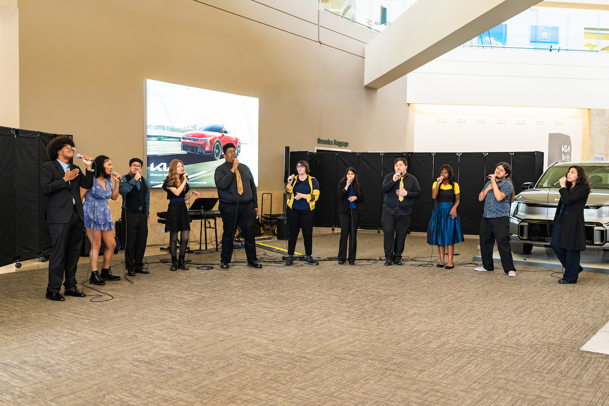 Choral students stand and sing in a row in the baggage claim area of John Wayne Airport.