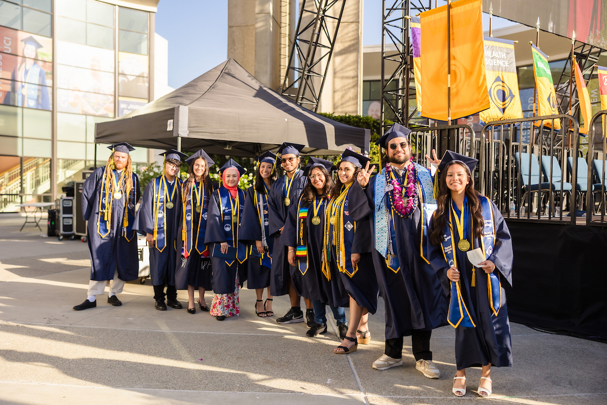 The nine Presidential Scholars of Distinction pose in commencement regalia in front of the commencement stage
