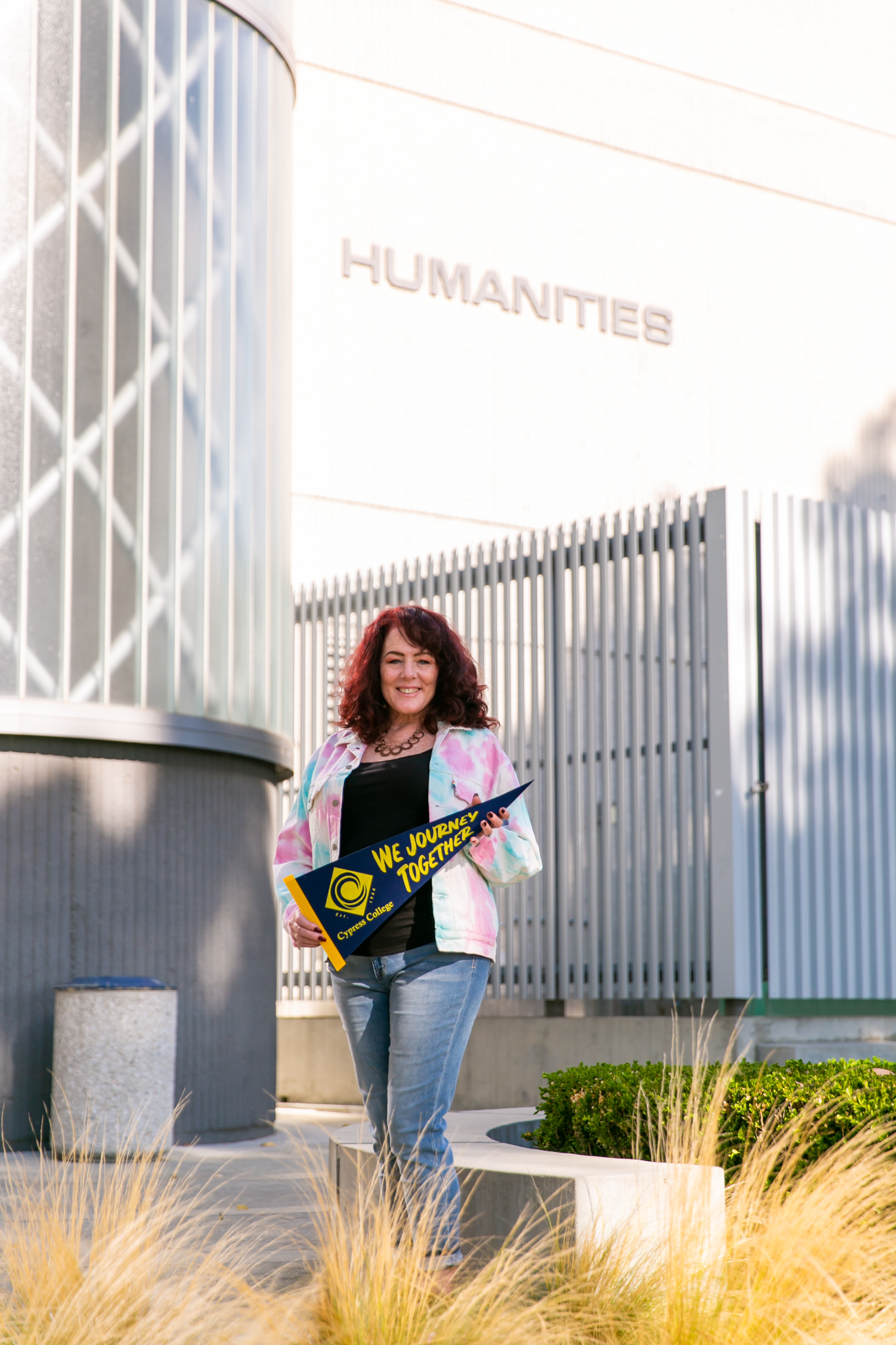 Lisa Plechner poses with pennant in front of Humanities building on Cypress College campus. 