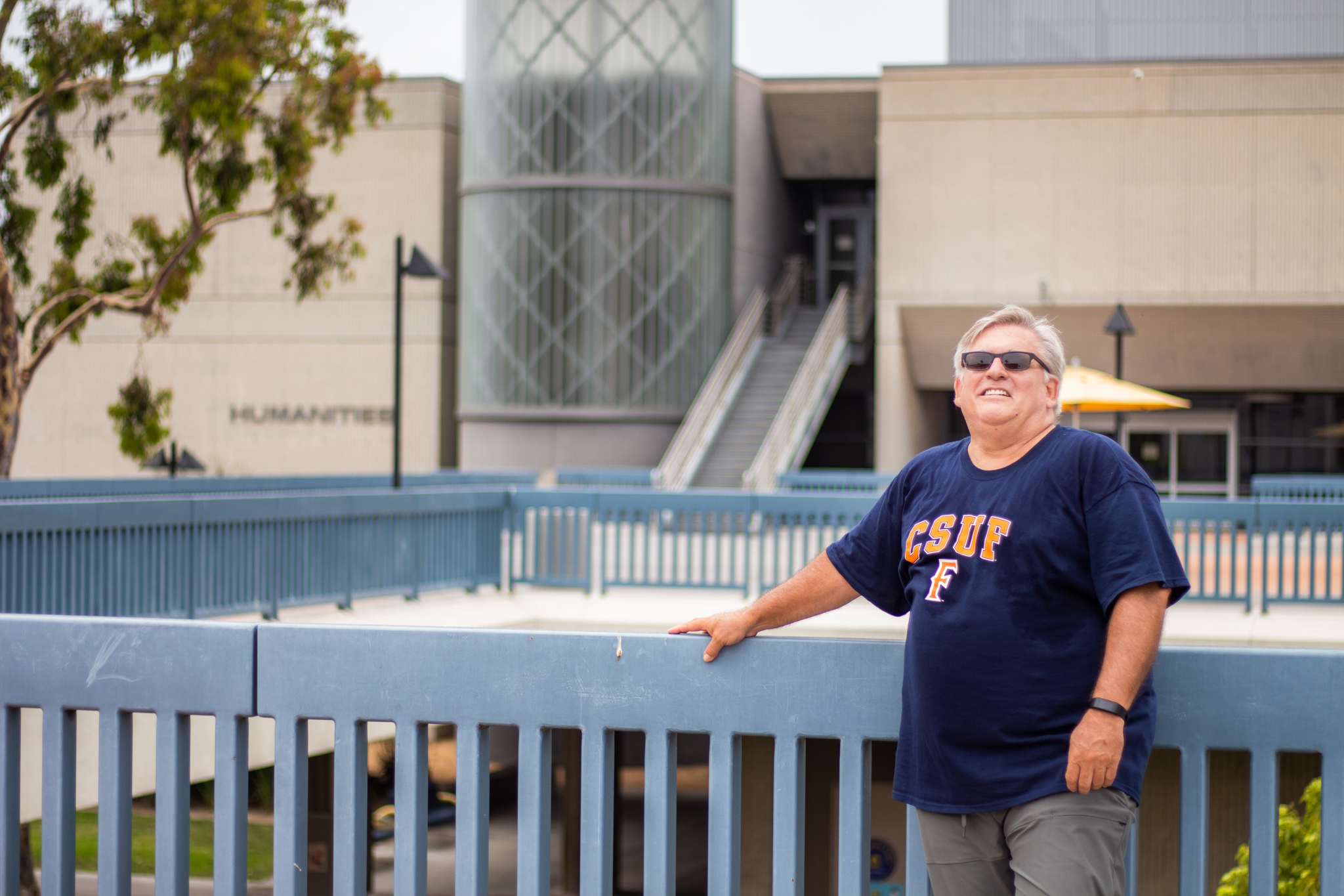 Patrick Hale, an older white man with silver hair, poses on second level piazza at Cypres College.