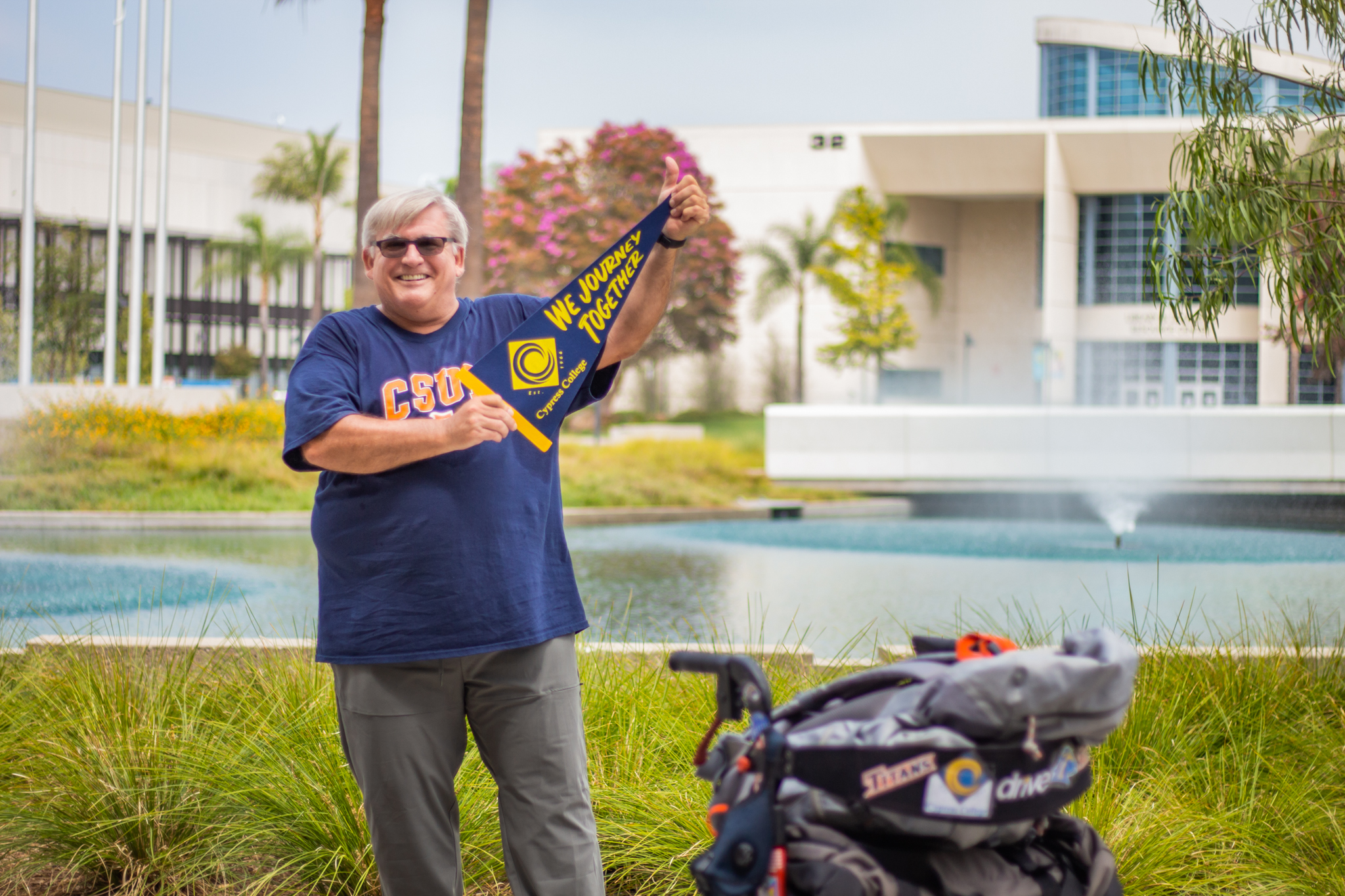 Patrick Hale proudly holds a Cypress College banner as he stands in front of the campus pond with his walker at his side.