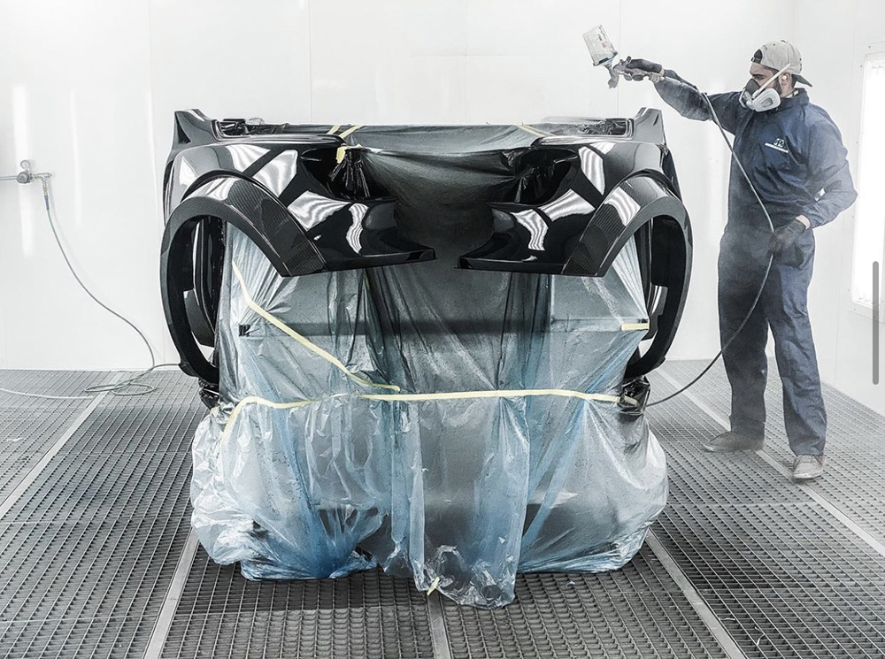 A man in coveralls and respiratory protection gear air brushes part of a car body.