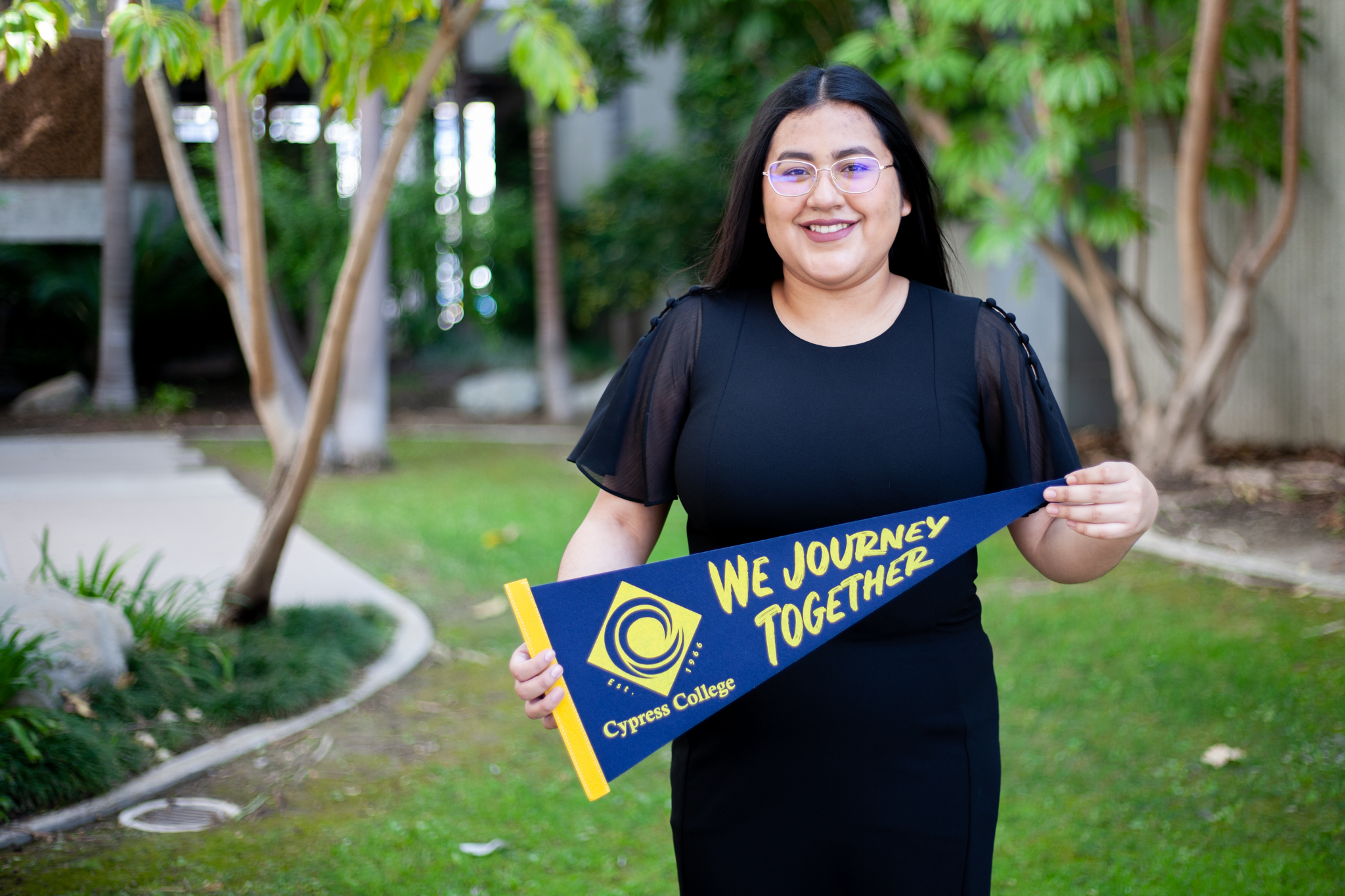 Abigail Villegas, health science student, holds a Cypress College pennant on the campus grounds. 