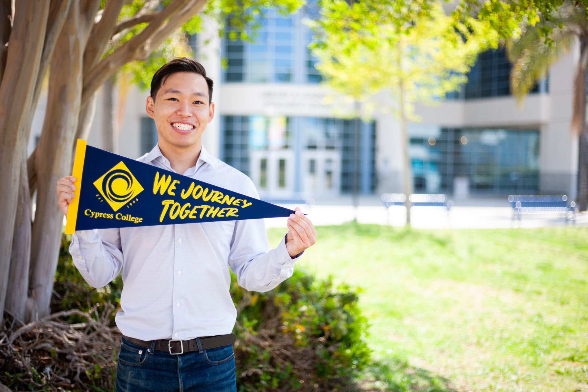 Student Hiroki Funahashi poses with Cypress College "We Journey Together" pennant in front of library. 