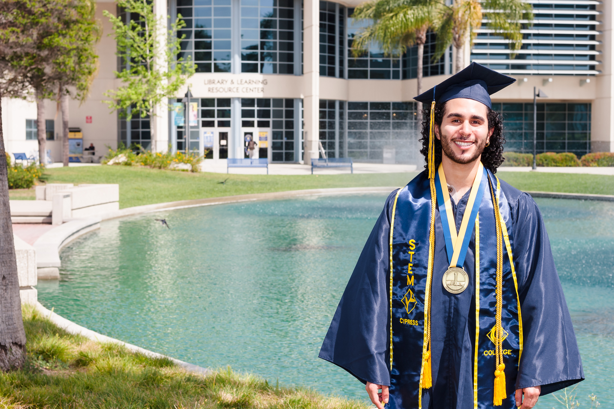 Student Justin Urquilla poses in front of library wearing Cypress College graduation regalia.