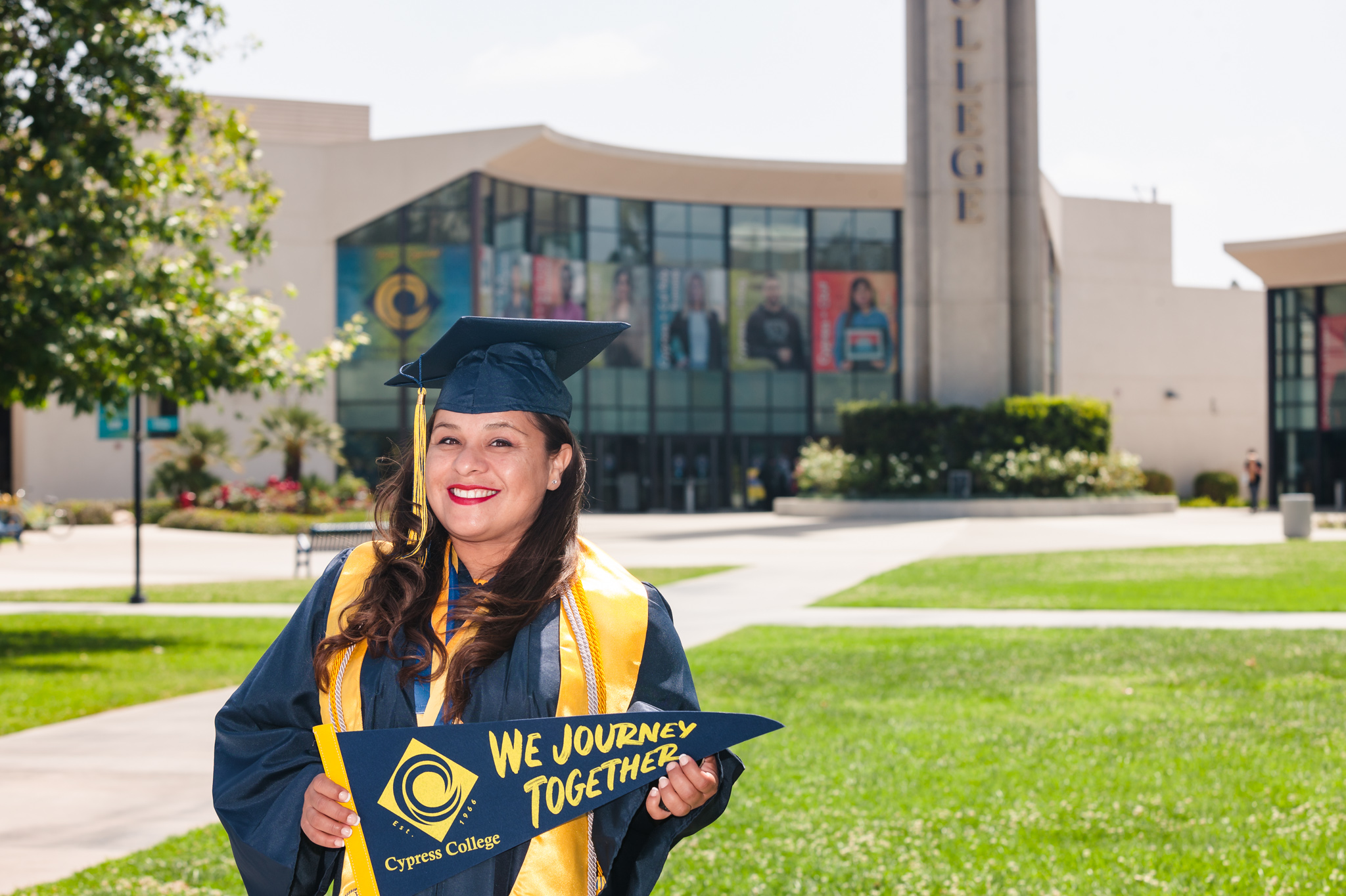 Student Mireya Alt poses in front of Cypress College Student Center while wearing graduation regalia.