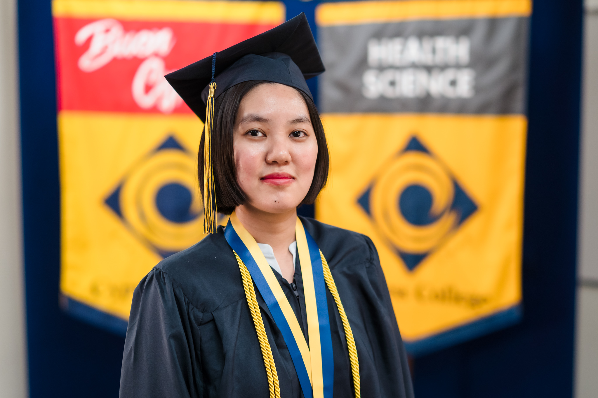 Student Pauline Lim poses with "We Journey Together" pennant as she wears graduation regalia and stands on the piazza.