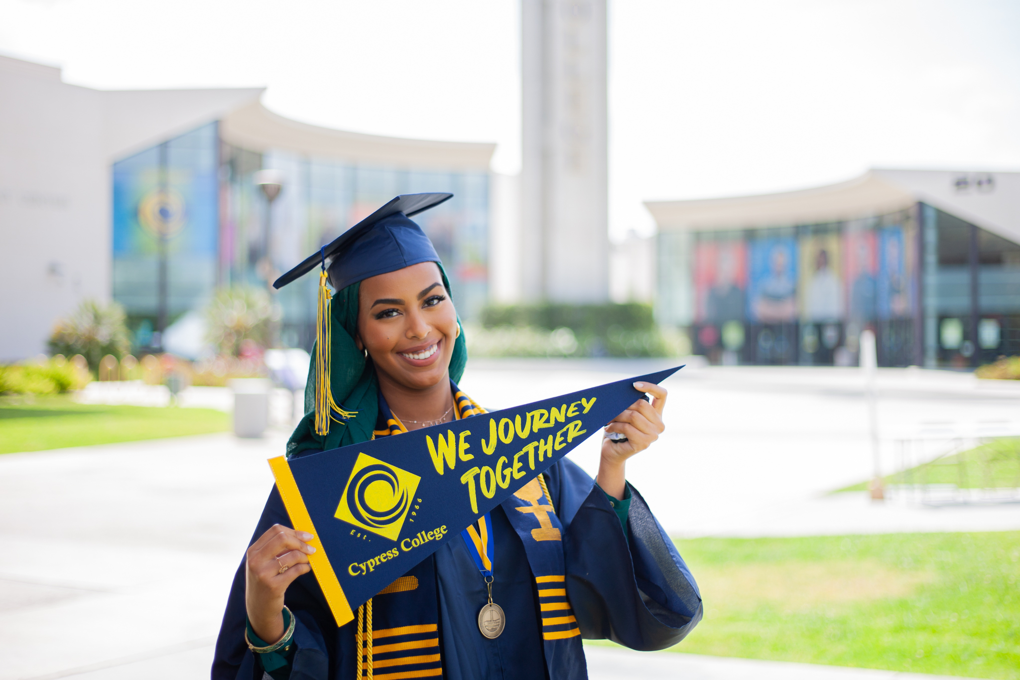 Student Ayah Said holds a Cypress College pennant in front of the Campanile. 