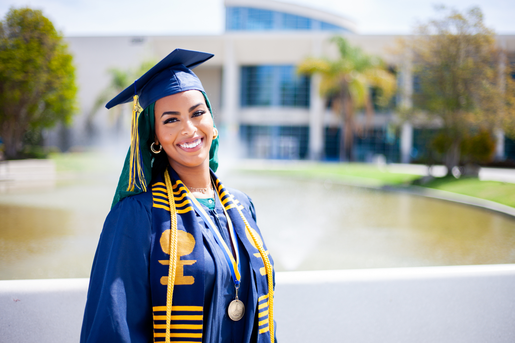 Counseling student Ayah Said in graduation regalia in front of the Cypress College pond. 