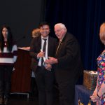 Student receiving a scholarship award and Dr . Schilling and a female student in a red and white sweater looking on.