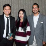 Smiling young woman with black hair and red and white striped sweater with two smiling young men in suits.