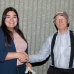 A young woman with long hair shaking hands with a gentleman wearing a cap, striped shirt and suspenders.