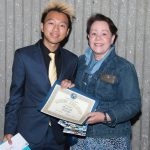 A young man in a suit and tie with blond hair, standing with a woman with short brown hair and a blue denim jacket.