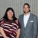 A young woman with glasses and long dark hair standing with a young man wearing glasses and a suit.